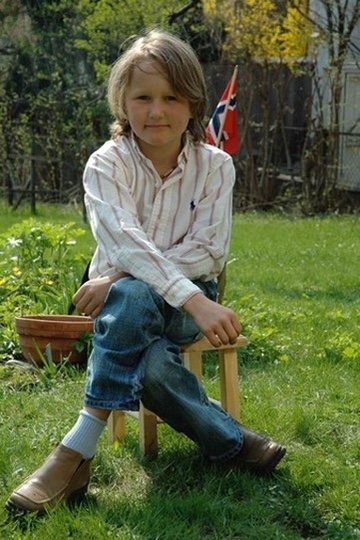 August som gutt, sittende på en krakk i en hage med et norsk flagg bak seg